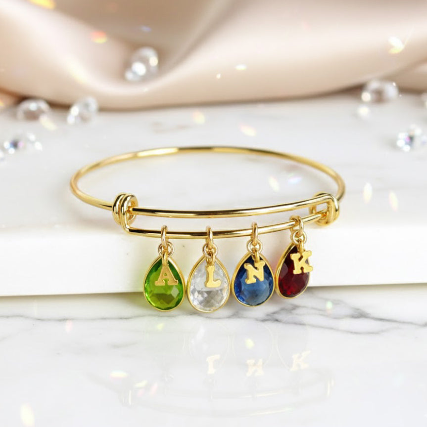 Gold bangle with plain style initial charms, letter charms and peridot, moonstone, kyanite and garnet birthstones. august birthstone, june birthstone, september birthstone, january birthstone 