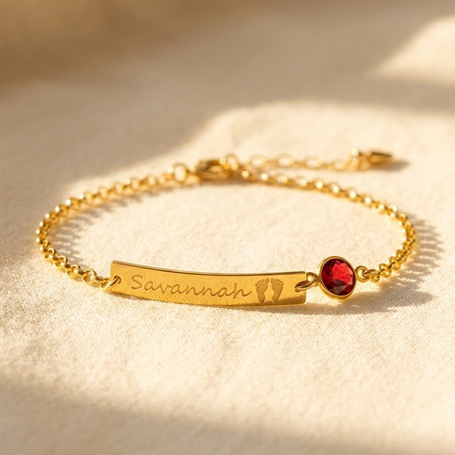 Personalized baby footprint bracelet with garnet January birthstone in gold finish. Custom engraved bar with name and footprint symbol, dainty chain design. Keepsake jewelry gift for moms, grandmothers, and new mothers. Perfect push present, baby shower, First Christmas or Mother’s Day gift. Handmade in sterling silver, gold, or rose gold with 6mm gemstone bezel.