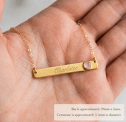 Custom name and birthstone bar necklace displayed in a hand with engraved personalization and gemstone accent.