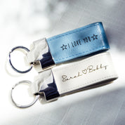 Two keychains at a diagonal angle rest on a textured cloth background. A silver blue keychain says I Love You in Sunshine font with stars on each side. A white keychain says Sarah (heart) Bobby in Grace font.Leather Keychain White Blue Magenta Brown Zinc Alloy Metal Keyrings Personalized Gift Personalized Key Fob College Dorm Gift College Grad Gift Graduation Gift for Him or Her Natural Leather Custom Gift for Women, leather anniversary gift, leather wedding anniversary gift, 3rd anniversary gift