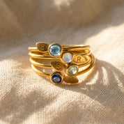 Stackable birthstone initial rings in gold with 3mm faceted gemstones and stamped leaf charms, personalized for family, mom, or couples.