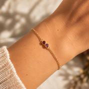 Gold two birthstone bracelet with garnet and amethyst worn on wrist
