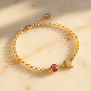 Gold filled double leaf charm with initial engraved and ruby birthstone on a white background. Ruby gemstone charm name