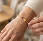 Woman wearing custom birthstone bracelet with engraved initial double leaf charm, delicate gold personalized bracelet for everyday wear or meaningful gift