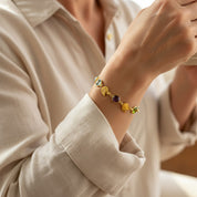 Woman wearing custom birthstone bracelet with engraved initial leaf charms, personalized mom bracelet in gold