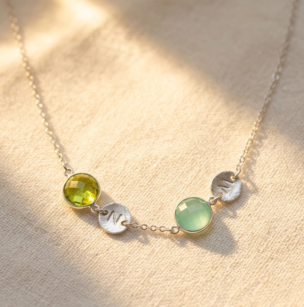 Custom birthstone necklace with initial charms hanging in natural light