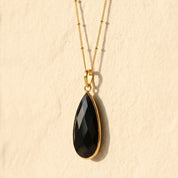 Black Onyx teardrop pendant necklace layered on delicate gold chains against a neutral background.