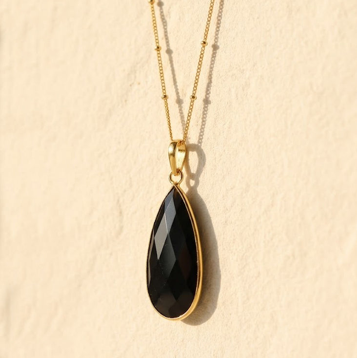 Black Onyx teardrop pendant necklace layered on delicate gold chains against a neutral background.