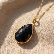 Close-up of black onyx teardrop necklace in gold vermeil, faceted black gemstone pendant necklace for women, dainty minimalist black stone jewelry, elegant everyday necklace, gift for her, polished bezel set onyx pendant with cable chain, timeless fine jewelry inspired black gemstone necklace for modern layering and classic styling