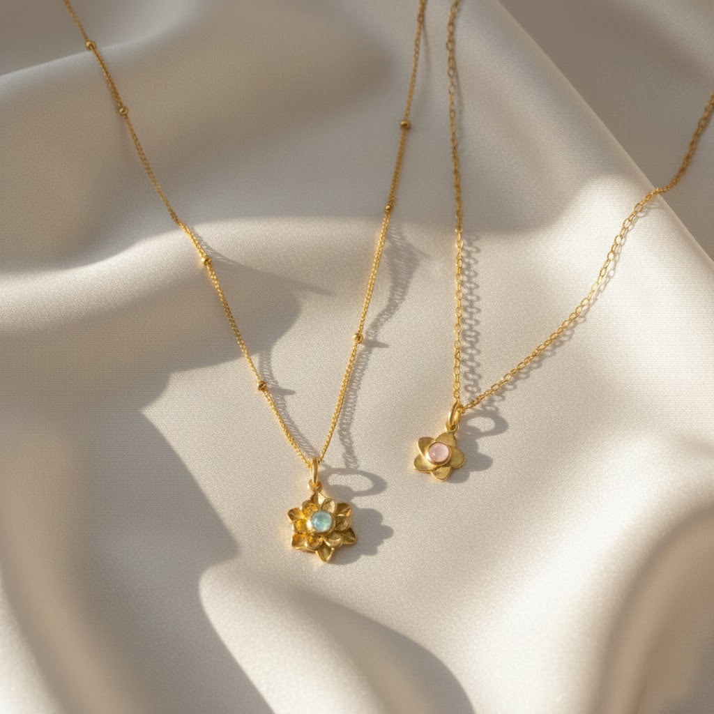 mother daughter birthstone flower necklace set with two gold bloom pendants resting on soft champagne satin, larger layered flower pendant with aqua blue center stone and smaller dainty blossom with pale pink birthstone, both on delicate gold chains catching warm sunlight, personalized birthstone flower necklaces available in sterling silver or gold filled, meaningful matching jewelry gift for mom and daughter, grandma and granddaughter, birthday, Mother’s Day or holiday