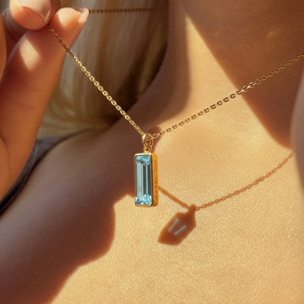 blue topaz vertical bar necklace worn by a woman in natural sunlight, showcasing the faceted december birthstone pendant hanging from a delicate gold chain, minimalist and elegant adira series birthstone jewelry perfect for everyday wear, december birthday gifts, christmas presents, or meaningful keepsake jewelry, customizable with engraving in sterling silver or gold vermeil for moms, daughters, sisters, or girlfriends