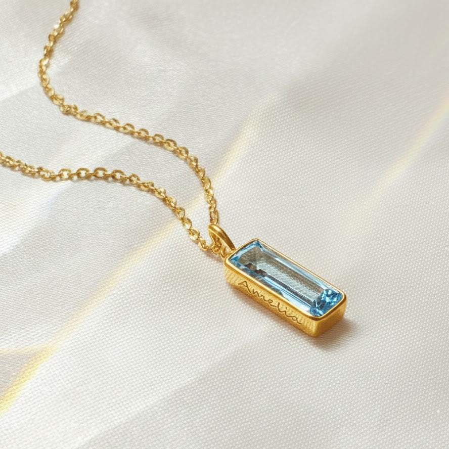 Single gold filled satellite chain with vertical sky blue gemstone with secret message engraved december birthstone adira bar necklace on white background