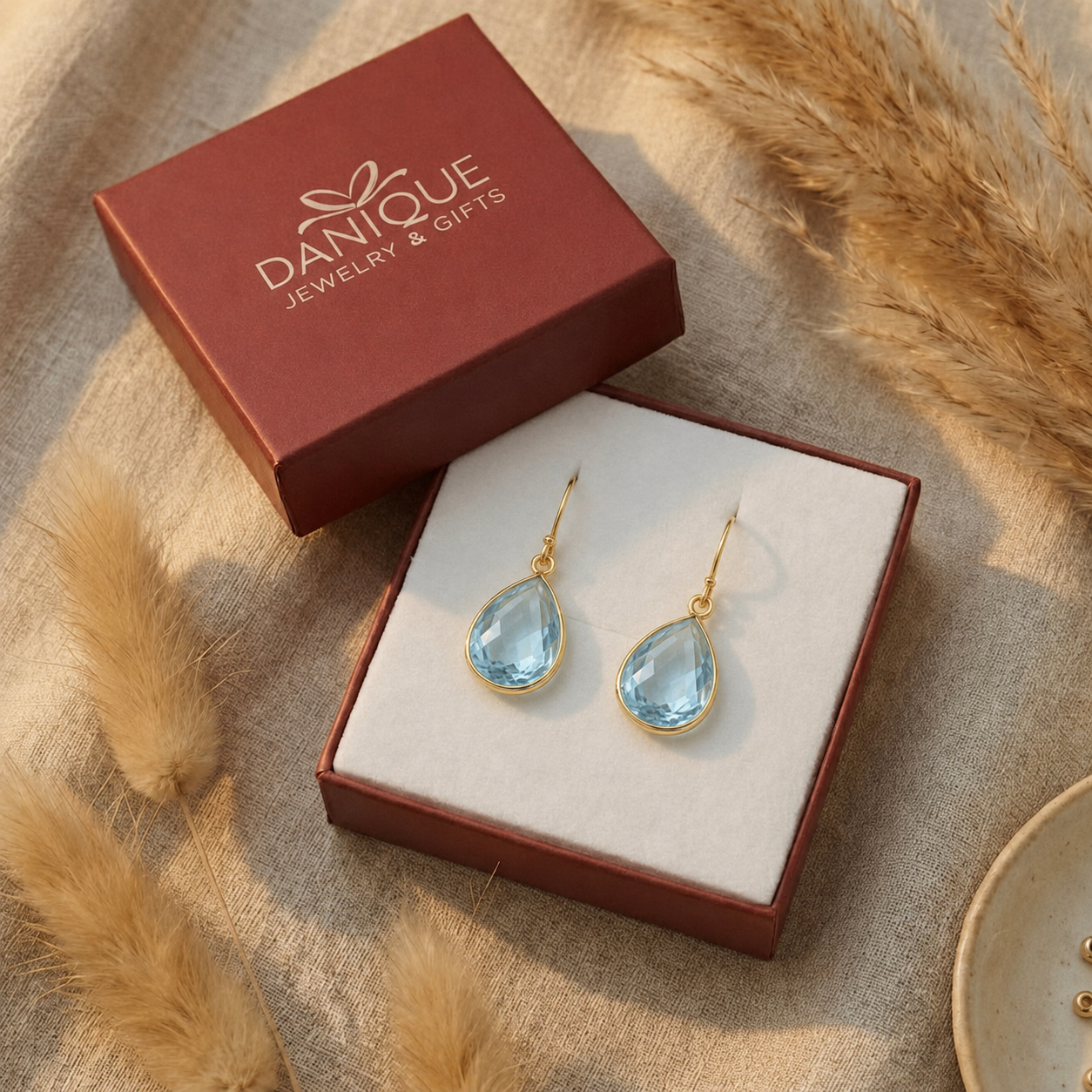 Blue topaz drop earrings presented inside an open red Danique Jewelry gift box.