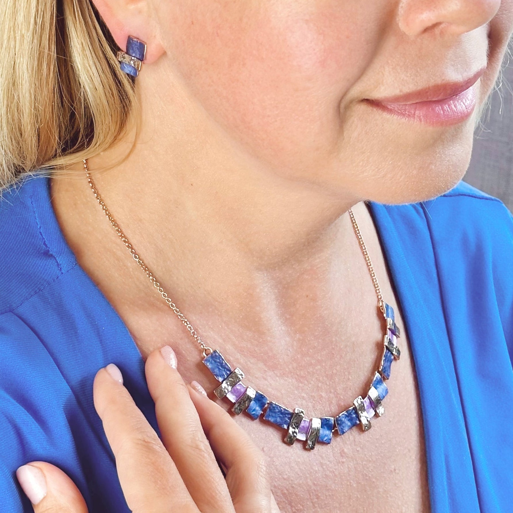 Pair of rose gold plated earrings with three textured stacked squares and matching necklace with rose gold, purple and pink square and rectangle pendants worn by a blonde model wearing a blue blouse