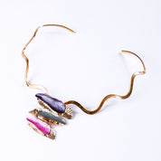 Necklace with a copper wavy neck ring and a rose gold plated pendant made of three sets of two overlapping long organic bar shapes with the top painted in enamel of either purple, gray, or pink. Necklace sits against a white background.
