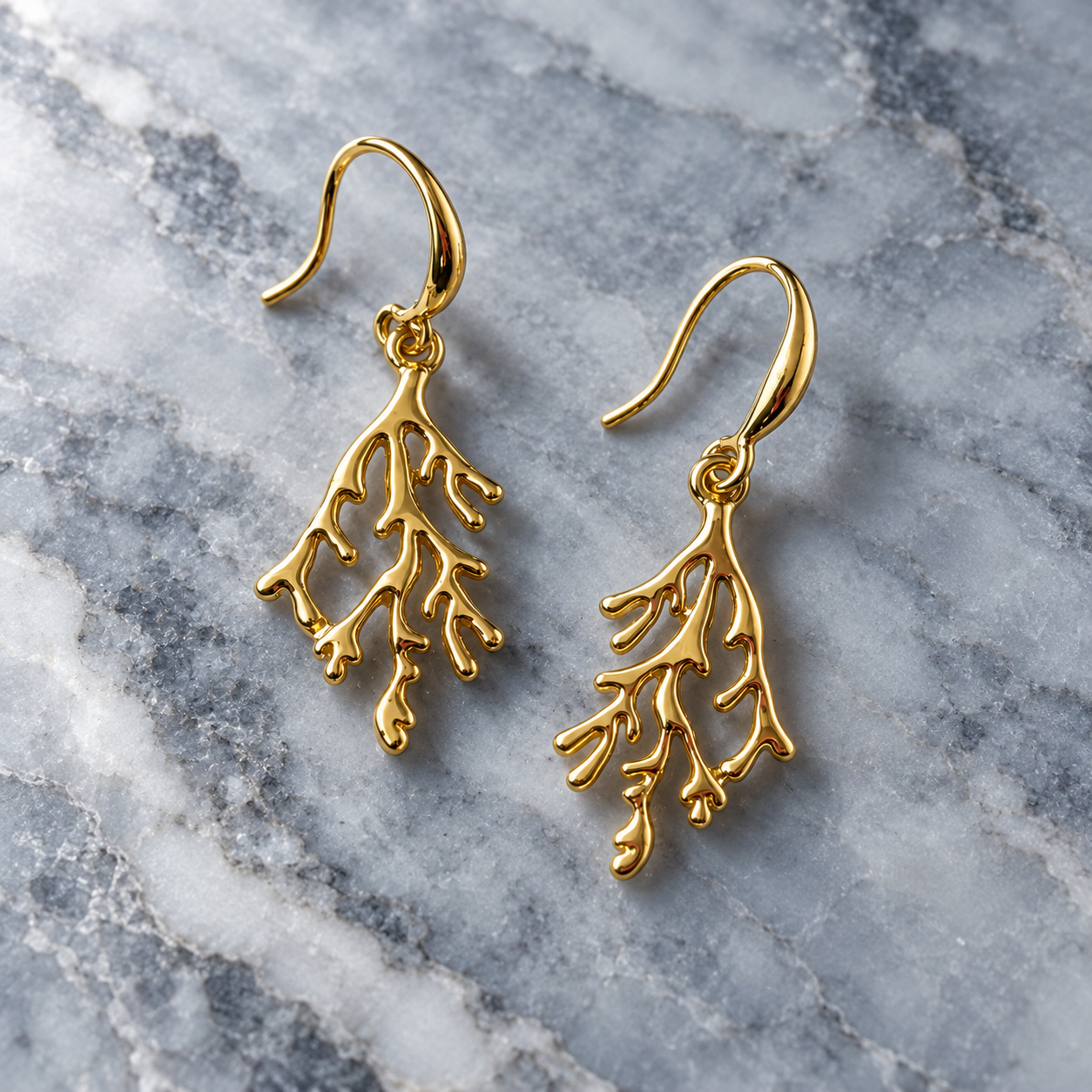 Gold coral branch hook earrings displayed on light marble background

