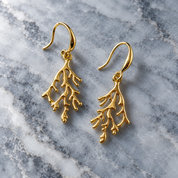 Gold coral branch hook earrings displayed on light marble background


