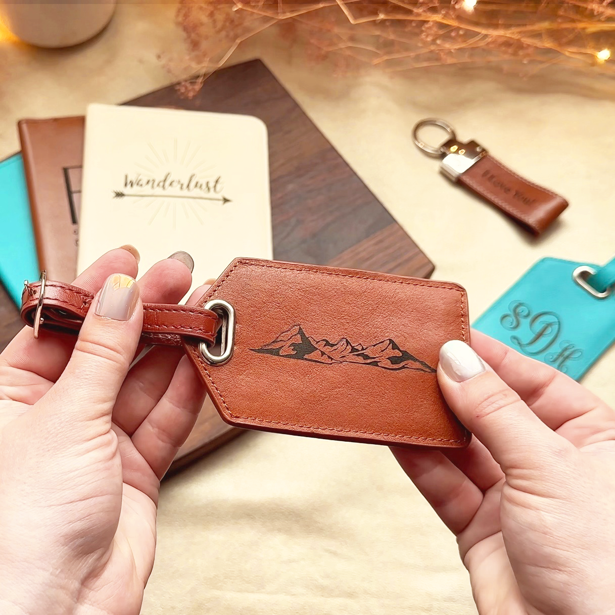 Two hands hold a cinnamon colored leather luggage tag. The engraving shows the outline of a mountain ridge. Personalized bridesmaid gifts, destination wedding party favors, destination wedding gifts, personalized guest gifts for wedding, travel wedding, travel gift, travel group, personalized leather travel accessories for group, bulk order, wholesale available, fast shipping, fast turnaround, fast production, 1-2 day delivery, 1-2 day production