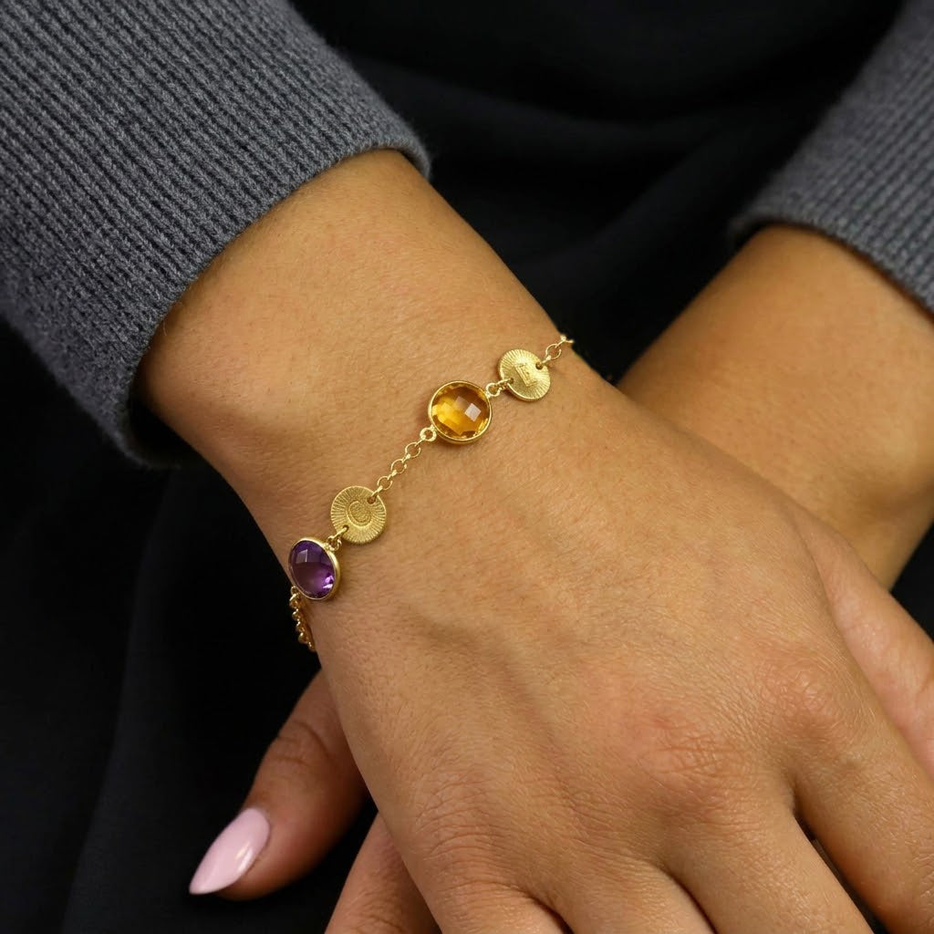 A person wearing a pink chiffon dress and a white sweater wears a silver brushed disc initial bracelet with a round peridot august birthstone and a sky blue topaz december birthstone. This bracelet can be made with any number of birthstones and initials. Matching necklaces are also available. Bracelets available in 14k gold fill with 18k Vermeil Gold parts or 925 Sterling Silver. Bracelets are perfect for Mother's Day, Christmas, or Birthdays for mom or grandma. 