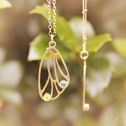 Gold butterfly wing necklace with blue birthstone and key charm hanging from branch, symbolic custom birthstone jewelry for nature and butterfly lovers