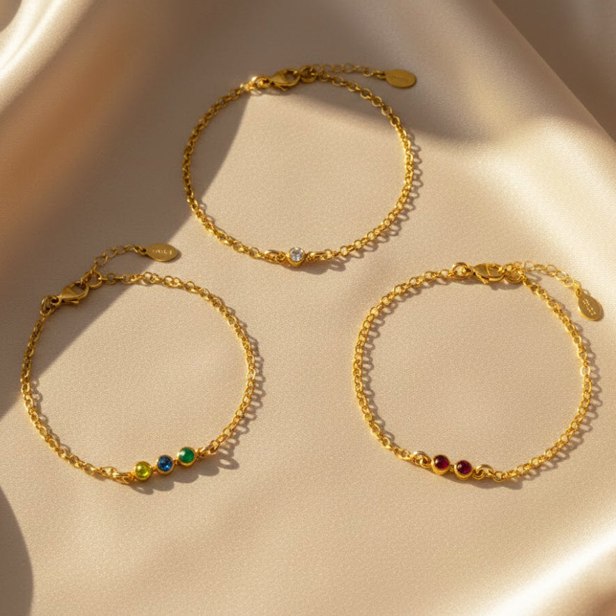 Set of three tiny cabochon birthstone bar bracelets displayed flat on champagne satin, mixed metal chains with colorful stones, customizable family birthstone bracelet stack, thoughtful gift for Mother’s Day, birthdays, anniversaries or Christmas.