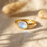 Oval moonstone ring worn on a model’s hand in natural sunlight with a minimalist gold band.
