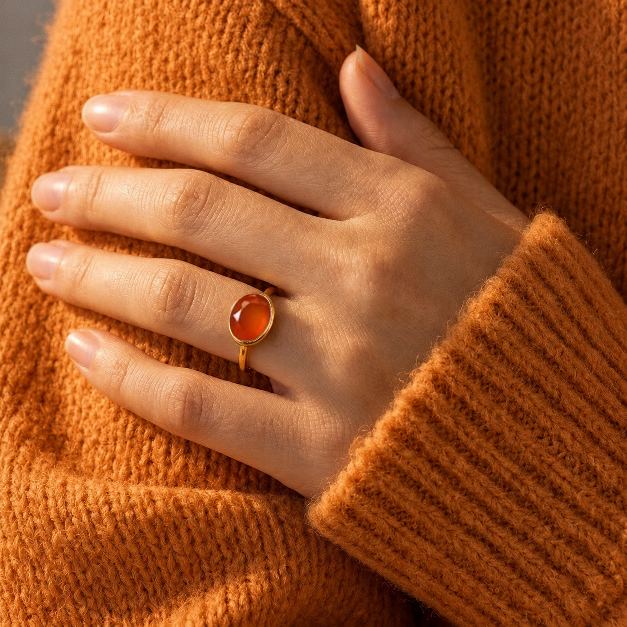 Woman wearing an oval carnelian gemstone ring in yellow gold vermeil with a warm orange sweater in natural sunlight.