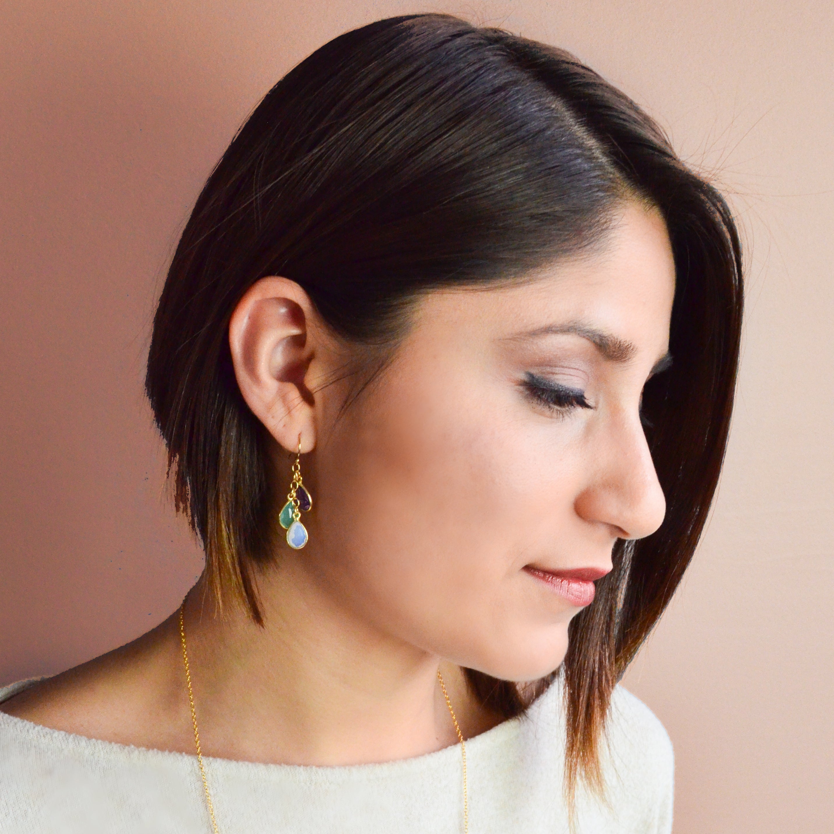 Model is wearing gold cascade earrings with purple amethyst, green onyx and moonstone.