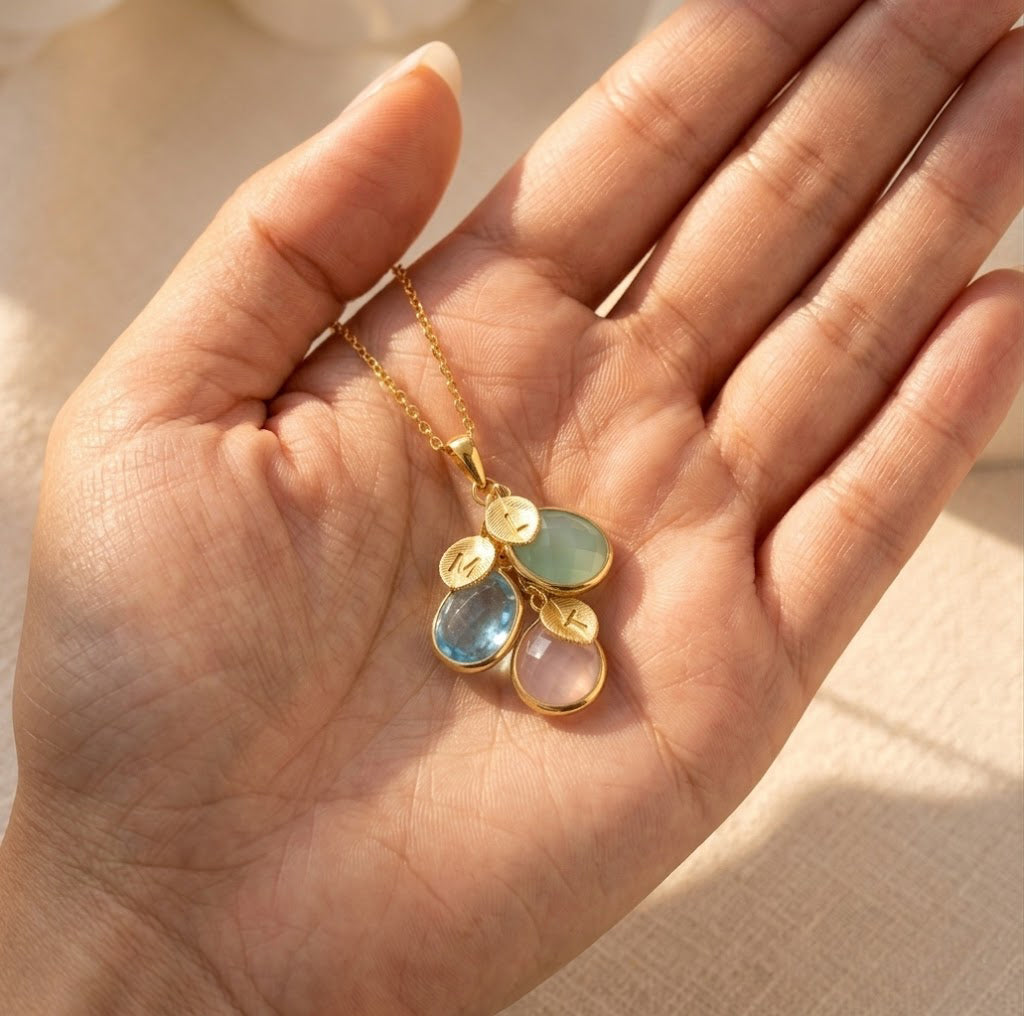 Custom birthstone necklace held in hand, showing cascading teardrop gemstones and initial charms for personalized mother’s jewelry.