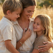 Smiling young mom wearing a custom birthstone mom necklace while playing with her child in a cozy sunlit living room, showing how the gold filled chain and clustered teardrop birthstones with engraved name charms sit at the perfect everyday length. Meaningful personalized family necklace with kids’ birthstones, a sentimental Mother’s Day, birthday or Christmas gift for mom, new mom or grandma.
