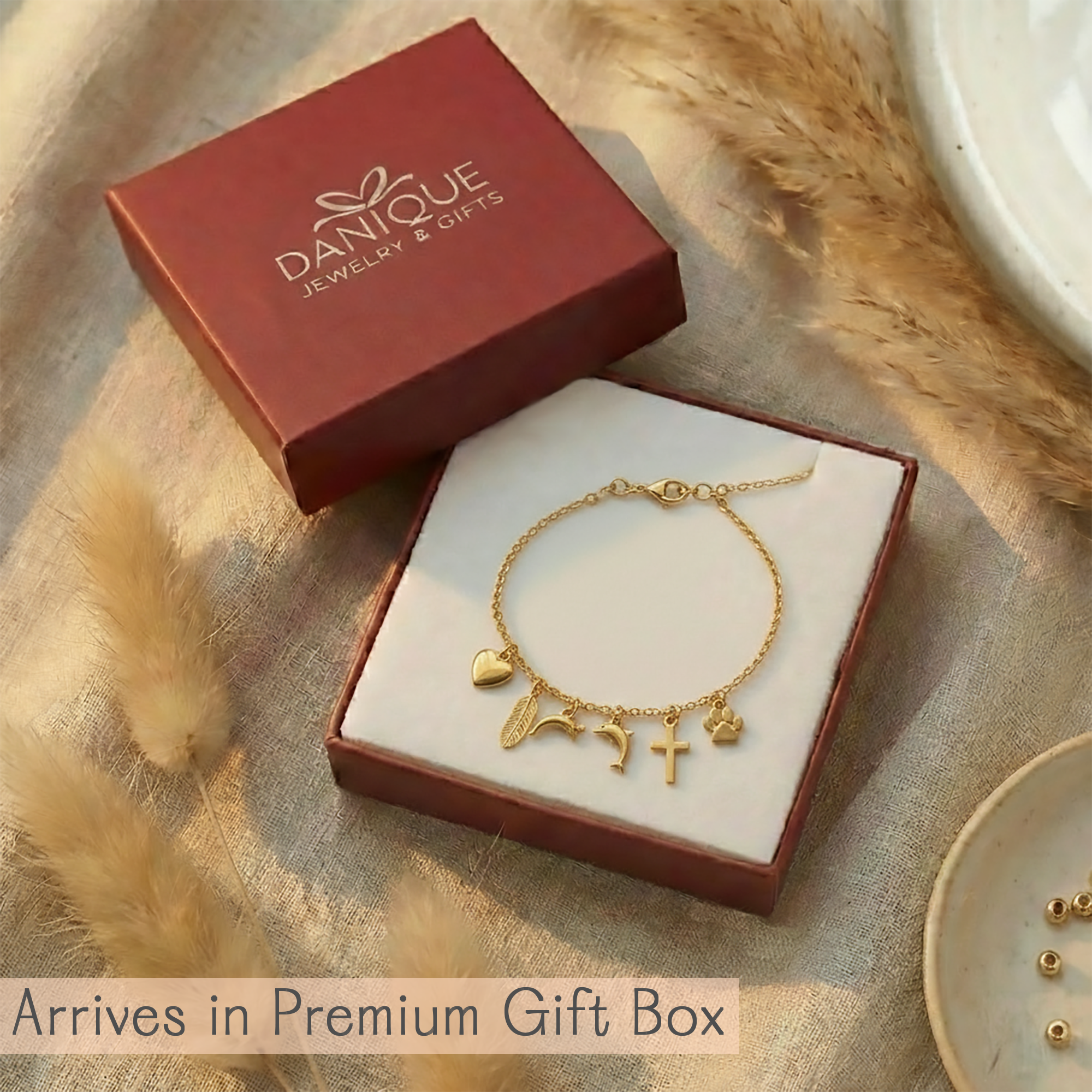 Gold bracelet with charms in a 'DANIQUE' jewelry box on a textured surface.