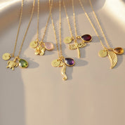 Custom angel wing necklaces with various birthstone colors and initial charms shown together, a thoughtful sympathy or remembrance jewelry collection for gifting.