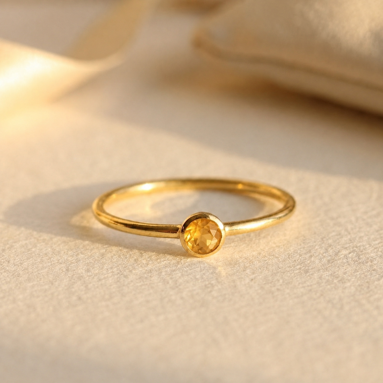 Dainty tiny round citrine ring in gold on soft cream fabric