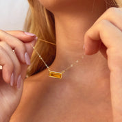 citrine baguette necklace shown on model holding the delicate gold filled chain and vertical bar pendant, sparkling yellow citrine gemstone catching sunlight, personalized engraving available on the bar pendant, dainty November birthstone necklace ideal for women who love minimalist jewelry, elegant layering piece and thoughtful personalized gift for her birthday, graduation or holiday season presented in premium packaging