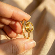 Lifestyle photo of a woman wearing an oval citrine ring stacked with other minimalist gemstone rings, showcasing a dainty gold band and bezel-set yellow citrine. Elegant birthstone stacking ring styled for everyday wear, personalized jewelry looks, and modern layering. Thoughtful gift for mom, wife, girlfriend, or best friend, ideal for November birthdays, anniversaries, Valentine’s Day, Mother’s Day, and meaningful family jewelry collections.