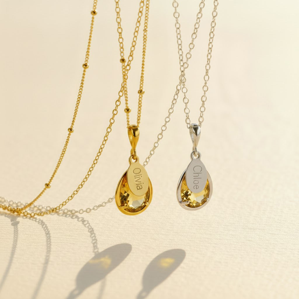 Citrine November birthstone necklaces shown in both .925 sterling silver and 14k gold-filled, each featuring a prong-set teardrop citrine gem paired with a small oval name tag engraved in script, hanging from delicate satellite chains on a soft neutral background. Personalized citrine pendants make meaningful November birthday gifts for mom, grandma, daughter or best friend, a warm golden keepsake she can wear every day, layered or alone for a minimalist look.