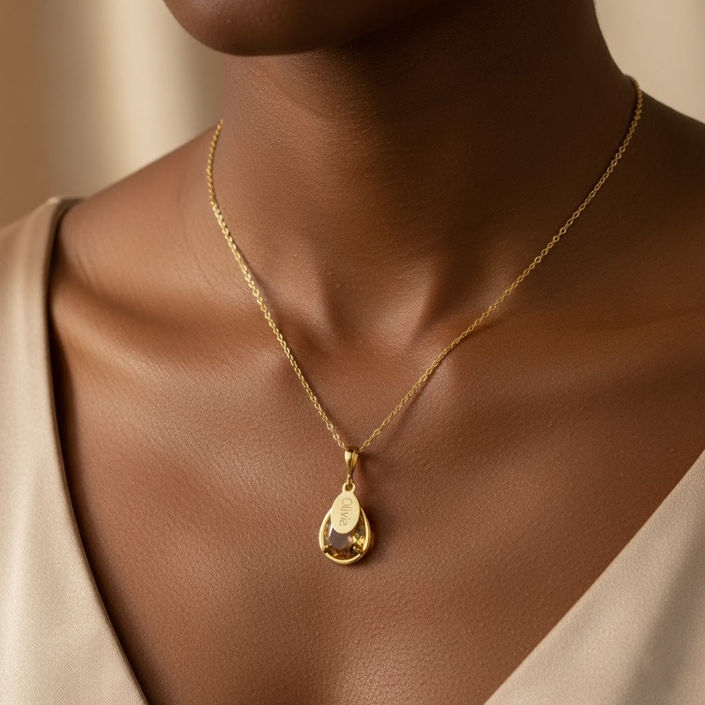 Woman wearing a personalized citrine November birthstone necklace with a prong-set teardrop gem and engraved name tag in script, elegant and minimal style perfect for everyday wear. Custom citrine pendant is an ideal November birthday gift for mom, daughter or grandma. Gold-filled finish adds warmth to the vibrant yellow gemstone. Available in sterling silver or gold-filled and engraved with any name for a meaningful keepsake.