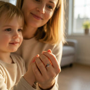 Lifestyle image of mom and child holding hands while mom wears a personalized birthstone ring, sentimental family jewelry symbolizing motherhood and children, custom mom birthstone ring with kids’ birth months, meaningful keepsake jewelry for Mother’s Day or grandma gift, handcrafted minimalist design inspired by June pearl and December blue topaz