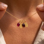 Personalized Mom birthstone necklace with oval gemstone charms and engraved children's name tags in yellow gold.
