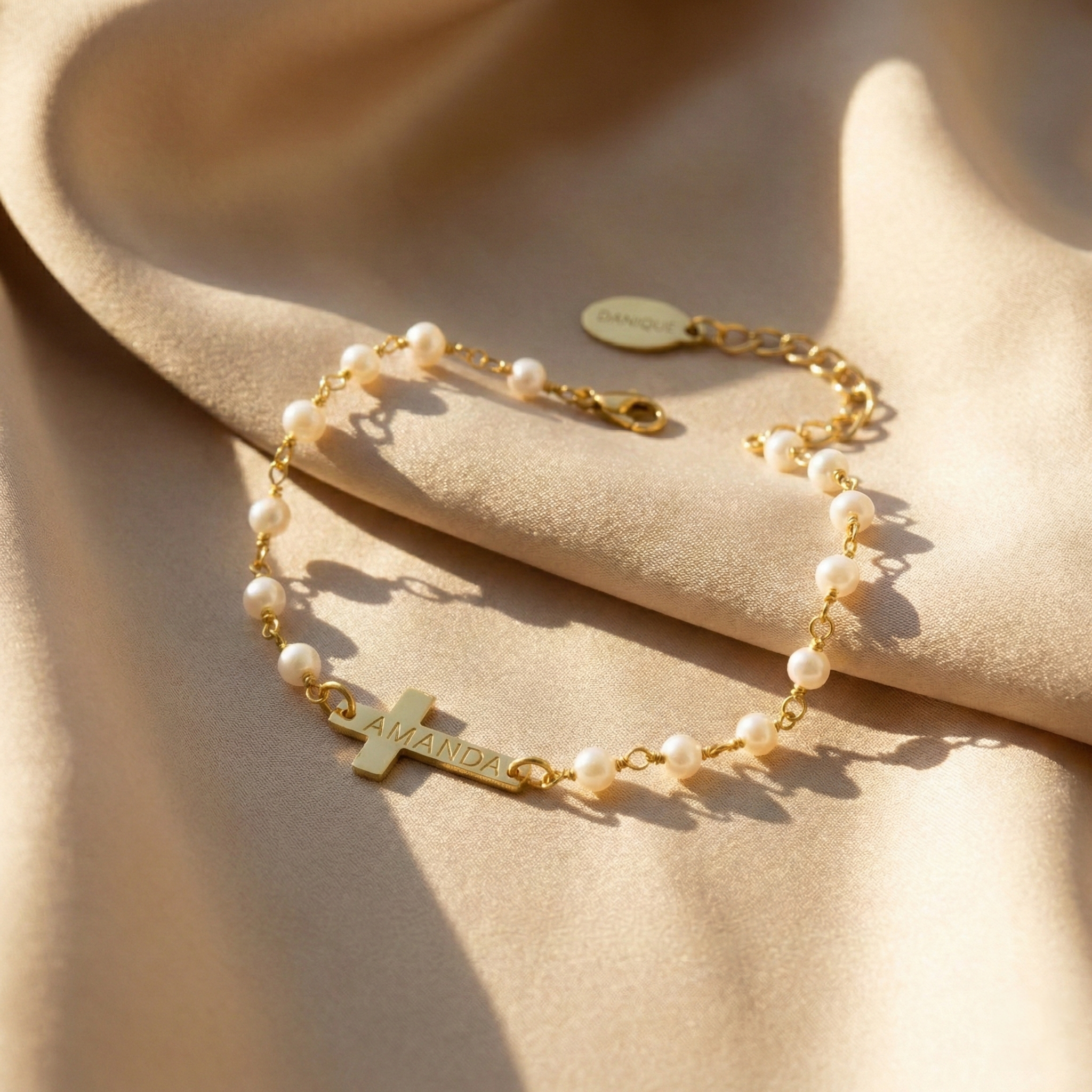 Pearl bracelet with a cross charm and engraved name on a beige background. This bracelet is perfect as a baptisms, christenings or first communion gift. It also makes a lovely Christian wedding gift.