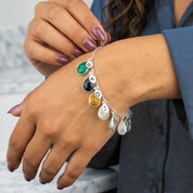 Close-up of custom birthstone bracelet with stamped initial charms, personalized gold family bracelet on wrist