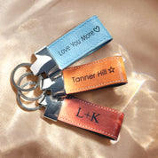 A trio of personalized leather loop keychains featuring engraved coordinates and heartfelt messages “I love you” and custom initials, shown on a natural stone background. These durable leather fobs with stitched edges and silver key rings make thoughtful location-based gifts, GPS memory keepsakes, or sentimental anniversary souvenirs. Handmade from premium full-grain cowhide in a Boston studio—ideal for couples, graduates, or travelers looking to carry a meaningful little piece of memory with their keys.