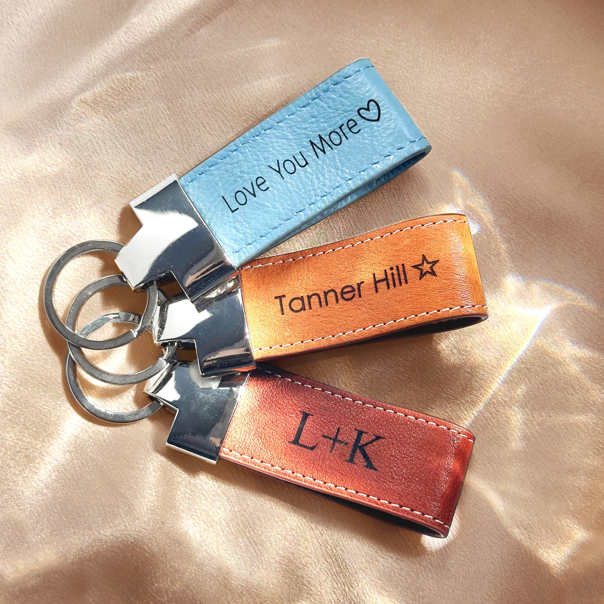 A trio of personalized leather loop keychains featuring engraved coordinates and heartfelt messages “I love you” and custom initials, shown on a natural stone background. These durable leather fobs with stitched edges and silver key rings make thoughtful location-based gifts, GPS memory keepsakes, or sentimental anniversary souvenirs. Handmade from premium full-grain cowhide in a Boston studio—ideal for couples, graduates, or travelers looking to carry a meaningful little piece of memory with their keys.