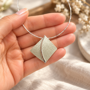 Hand holding Soft Pearl sculpted leaf pendant necklace showing textured pearlescent finish
