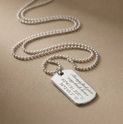Hand holding engraved sterling silver dog tag necklace and matching keychain