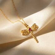 Gold dragonfly birthstone necklace closeup on soft beige fabric, dainty insect pendant with marquise wing stones and a center birthstone, personalized custom birth month jewelry in 925 sterling silver or gold vermeil, minimal everyday necklace gift for her, nature lover, birthday, anniversary, memorial keepsake