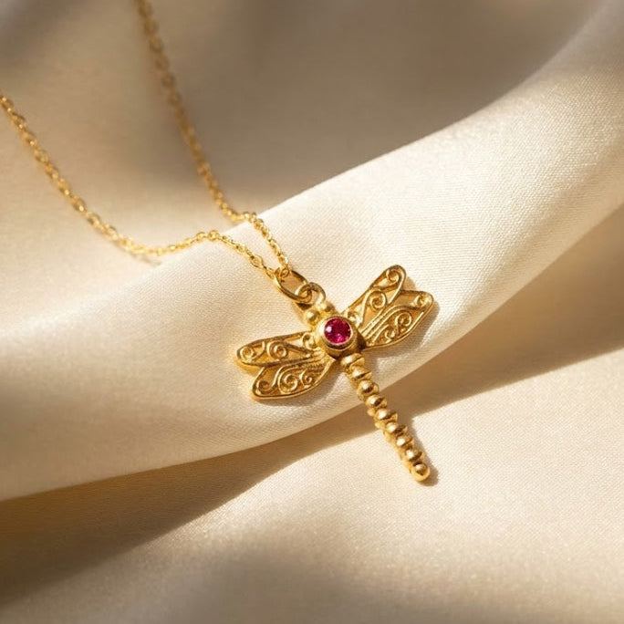 Gold dragonfly birthstone necklace closeup on soft beige fabric, dainty insect pendant with marquise wing stones and a center birthstone, personalized custom birth month jewelry in 925 sterling silver or gold vermeil, minimal everyday necklace gift for her, nature lover, birthday, anniversary, memorial keepsake