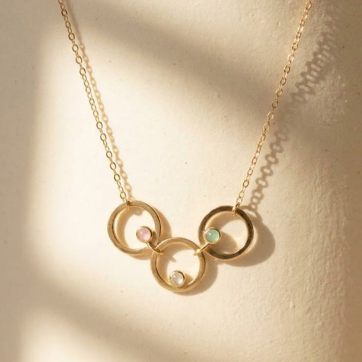 Three linked gold circle pendants with pink, aqua and clear birthstones on a delicate family necklace.
