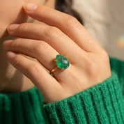 Woman wearing a natural emerald teardrop ring in yellow gold, showing the green May birthstone’s size and hand scale.