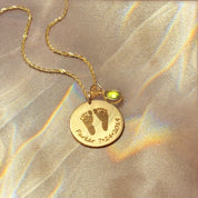 Personalized baby footprint necklace with engraved footprints, custom name, and birth date paired with a sparkling peridot birthstone charm. Meaningful keepsake jewelry for moms to celebrate a new baby, adoption, or to honor the memory of a child. Engraved disc pendant available in sterling silver, gold filled, or rose gold filled, making a heartfelt gift for Mother’s Day, baby shower, baptism, or angel baby memorial. This custom necklace keeps your child’s footprints close and is a timeless symbol of love,